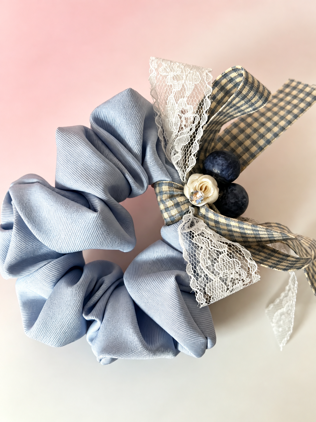 Close-up of blue gray fabric scrunchie with gingham and lace bow